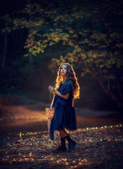 A girl in a blue dress looking at the sky and holding a glowing heart in her hands in the night forest