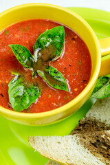 A cup of tomato soup with basil leaves and slices of bread on a green plate