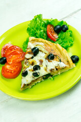 Slice of pizza on a green plate with vegetables