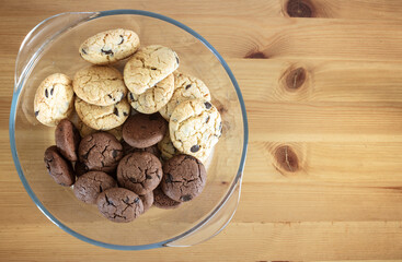 Top view of groups of white and brown chocolate chip cookies in glass bowl on wooden table with copy space.