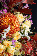 Fragment of a bright autumn bouquet in yellow-orange tones with roses and chrysanthemums on a black background.