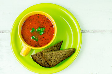 A cup of vegetable soup on a green plate with slices of bread