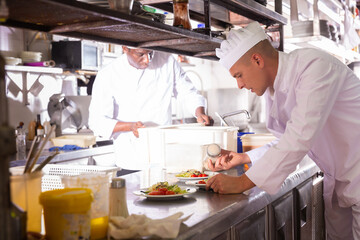 Fototapeta na wymiar Confident experienced chef in white uniform working in professional kitchen of restaurant