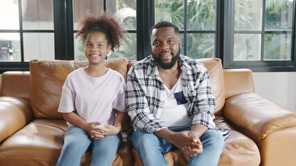 Happy African American family dad and daughter having fun cuddle and video call on laptop on sofa at house. Self-isolation, stay at home, social distancing, quarantine for coronavirus prevention.