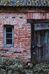 old orange brick wall with small tiny window and vintage wooden plank door with lock