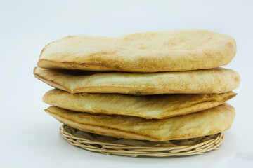 Fresh round pita bread on a clean white background. Flat unleavened white bread baked in a tandoor. Ready-made fresh pastries in the middle lies on a wicker tray.