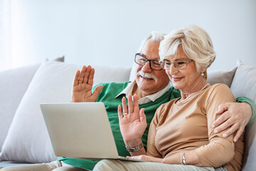 Portrait of smiling senior couple sitting together at home and surfing internet on laptop. Senior couple staying in touch with their family using their laptop at home