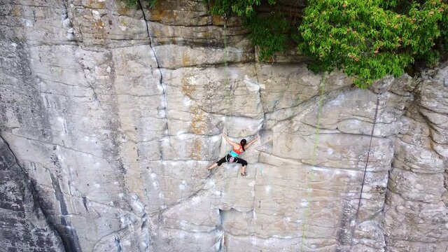 Girl rock climber climbs a limestone rock with a rope and a hook. Prepared climbing track.