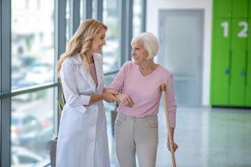 Positive doctor in a lab coat walking with a senior patient