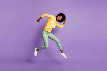Fototapeta na wymiar Full size photo of excited dark skin girl jump grimacing wear yellow pullover isolated over purple color background
