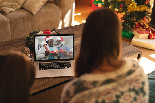 Rear view of woman and son having a videocall with senior couple in santa hats opening gift box on l