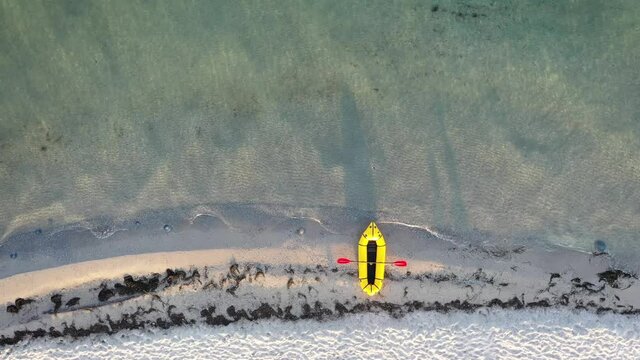 Yellow packraft rubber boat with red padle and turquoise water waves from top view. Beach with yellow sand glowing by sunlight. Travel summer vacations seascape background from drone