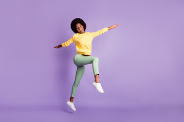 Fototapeta na wymiar Full size photo of excited dark skin girl jump up wear yellow sweater green pants isolated on purple color background
