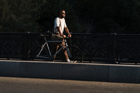 Happy african american guy smiling while walking with bicycle
