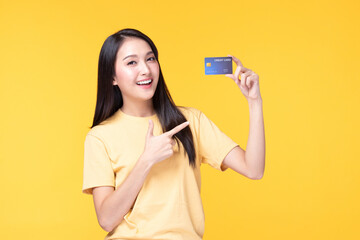 Cheerful young asian woman in yellow T-shirt holding bank card isolated on yellow background