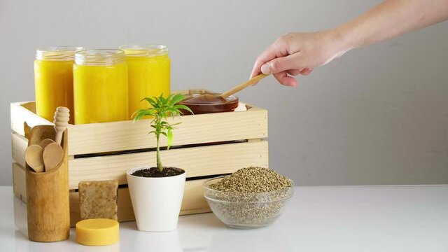Hand dripping CBD honey next to marijuana plant and hemp seeds