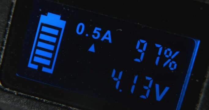 Screen of contemporary charging gadget with glowing blue digits and battery picture icon on black background extreme closeup