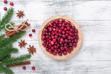 Raw fresh cranberries in wooden bowl, spice and fir branches on light wood background. Top view