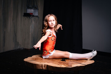 A little gymnast girl with curly hair and a red and white suit shows gymnastic exercises on a...