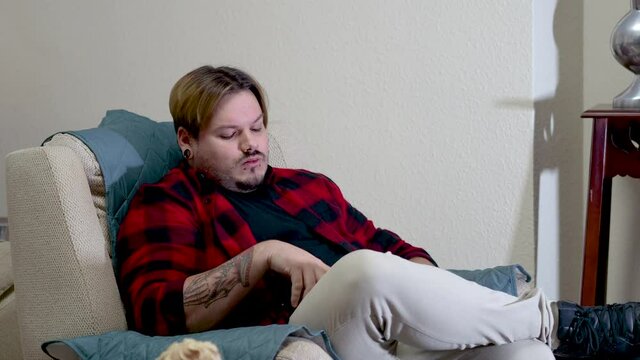 Hombre aburrido en el sof&aacute; con el m&oacute;vil y viendo la televisi&oacute;n estando confinado por la pandemia del coronavirus
