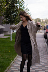 attractive slim young brunette in fashionable trench coat and black dress.