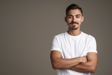 Fototapeta premium Image of pleased unshaven guy posing on camera with arms crossed