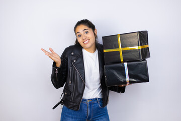 Young beautiful woman holding gifts over isolated white background clueless and confused expression...