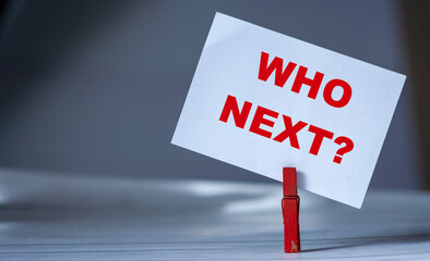 Reminder sticky note with clothes pin on table. Sticky note with inscription question WHO NEXT?...
