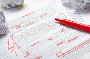 Closeup of text and red marks, crumpled pieces of paper and red marker on the desk.Process of...