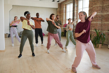 Group of people learning dance exercises with instructor in dance hall