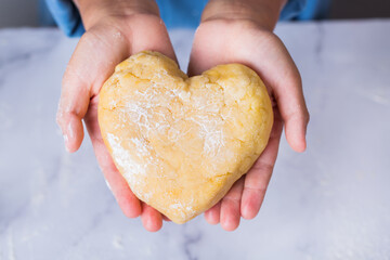 Cute boy holding in hands heart shaped piece of dough