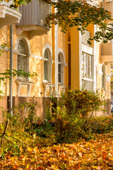 Facade of a yellow house in the Stalinist Empire style and golden fallen leaves, autumn day, vertical
