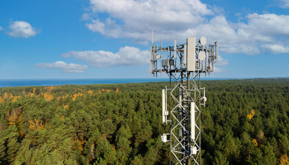 telecommunication tower with cellular antennas for 5g mobile internet network on forest and blue sky background