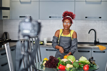 African american woman filming her blog broadcast about healthy food at home kitchen. She cuts a...