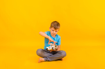 Fototapeta na wymiar the boy toddler is playing with a white car on a yellow background with space for text