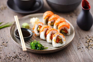 Sushi maki rolls with salmon, avocado, flying fish roe and cucumber on a plate with chopsticks, soy sauce, wasabi and ginger. Japanese traditional seafood served for lunch in modern gourmet restaurant