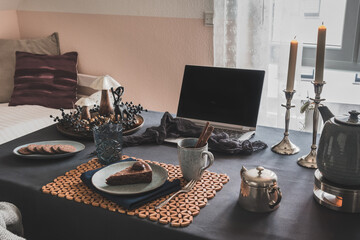 Table with laptop, cake, cookies and autumnal decoration in a cozy room prepared for virtual coffee...
