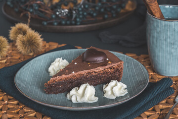 Piece of homemade chocolate pie with cream on a grey plate on a autumnal decorated table.