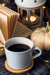 Cozy home interior. A knitted blanket lies on a soft gray chair with a book and a cup of coffee. Home holiday concept on a cold winter day.