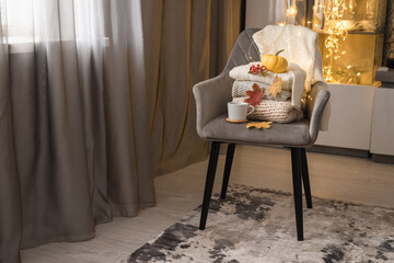 Still life in vintage style. Home interior. Knitted clothes are stacked on a gray chair. Home holiday concept on a cold autumn day. Lights, leaves, pumpkin.