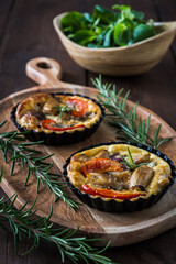 Two vegetarian tartlets on a wooden board and a wooden bowl with fresh field salad on a rustic table, vertical stock photo