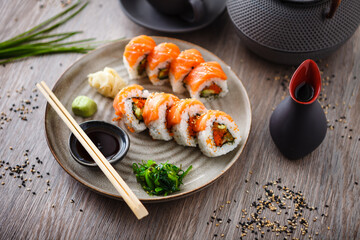 Sushi maki rolls with salmon, avocado, flying fish roe and cucumber on a plate with chopsticks, soy sauce, wasabi and ginger. Japanese traditional seafood served for lunch in modern gourmet restaurant