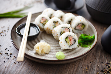 Sushi maki rolls California with crab, cucumber and avocado on a plate with chopsticks, soy sauce, wasabi and ginger. Japanese traditional seafood served for lunch in modern gourmet restaurant
