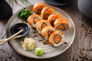 Baked sushi maki rolls with salmon, crab and spicy sauce on a plate with chopsticks, soy sauce, wasabi and ginger. Japanese traditional fish food closeup served for lunch in modern gourmet restaurant