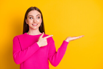 Photo of charming lady direct finger hold hand look empty space wear pink sweater isolated yellow...