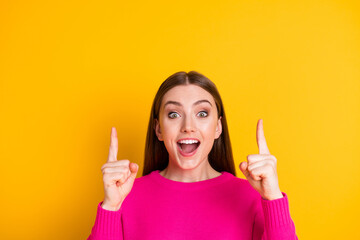 Photo of pretty girl direct fingers look up empty space amazed open mouth wear pink sweater isolated yellow color background