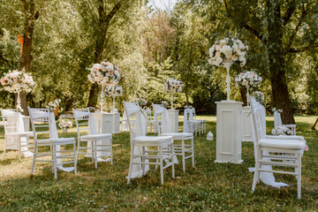 Wedding ceremony outdoors in the park. White chairs decorated with roses.
