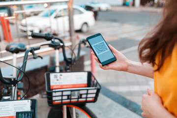 Bike rental on the street. A woman scans a qr code on a Bicycle using a smartphone. Hand close-up