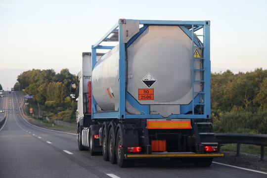 Gray semi truck tanker with 80/2586 dangerous class sign on barrel drive on asphalt highway on a summer day on green trees background, Arylsulfonic acids ADR hazardous cargo logistics, rear view