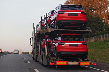 Loaded two level car carrier truck with car transporter semi trailer transportate chinese new red cars on suburban highway road, side rear view close up, delivery autos logistics transportation